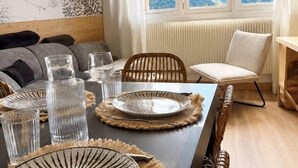 A dining area with a long table set for four, a view of mountains through large windows, and a rustic interior design. - The Marmots' Nest • Mountain View • 6 people (Orcières)