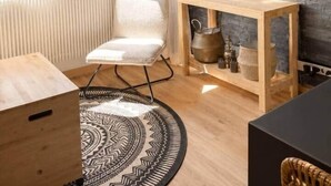 A cozy room with a wooden ceiling, a white chair, a wooden table, a TV mounted on a brick wall, and a view of mountains through large windows. - The Marmots' Nest • Mountain View • 6 people (Orcières)