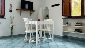 A dining area with a white table and chairs, a wall-mounted TV, a clock, and a bookshelf. - Casa Tasca, a cozy and quiet apartment with a large terrace. (Ravello)