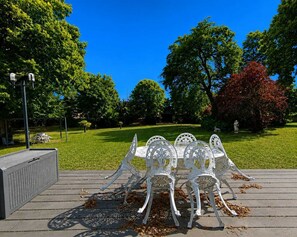 Espace extérieur aménagé avec une table et des chaises, une pergola et une zone herbeuse avec des arbres.
