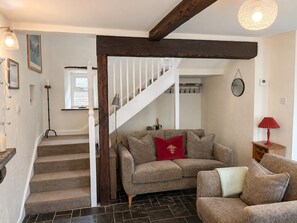 Eine Treppe führt zu einer zweiten Etage, einem Wohnzimmer mit Sofa, einem roten Kissen, einer Lampe und einem Spiegel an der Wand.