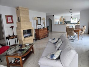 Ein Wohnzimmer mit Kamin, Sofa, Esstisch und Küchenzeile.