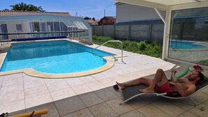 Une piscine entourée de parois en verre, une chaise longue et une terrasse carrelée.
