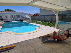 Ein Pool mit Glasveranda, Liegestuhl und gefliestem Sonnendeck.