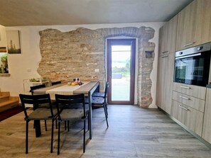 Una cocina con paredes de piedra, una mesa de comedor con sillas y vistas a través de un vano.