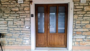 A stone wall entrance with a wooden double door, a welcome mat, and a number '2' on the wall. - Apartment Casa Sossa 2 (Umag)