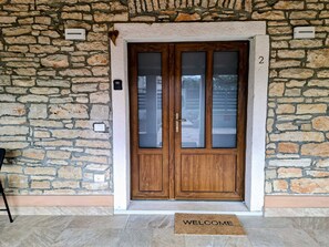 A stone wall entrance with a wooden double door, a welcome mat, and a number '2' on the wall. - Apartment Casa Sossa 2 (Umag)