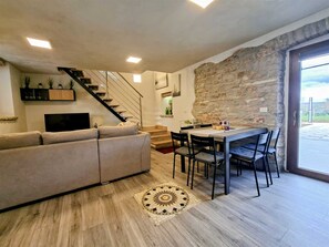 A modern living room with a sofa, dining table, chairs, a staircase, and a stone wall. - Apartment Casa Sossa 2 (Umag)