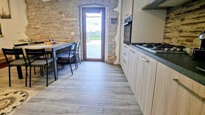 A kitchen with a stone wall, a dining area with chairs and a table, and a view through a doorway. - Apartment Casa Sossa 2 (Umag)