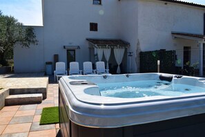 A hot tub in a courtyard with a white building, chairs, and a small garden area. - Apartment Casa Sossa 2 (Umag)