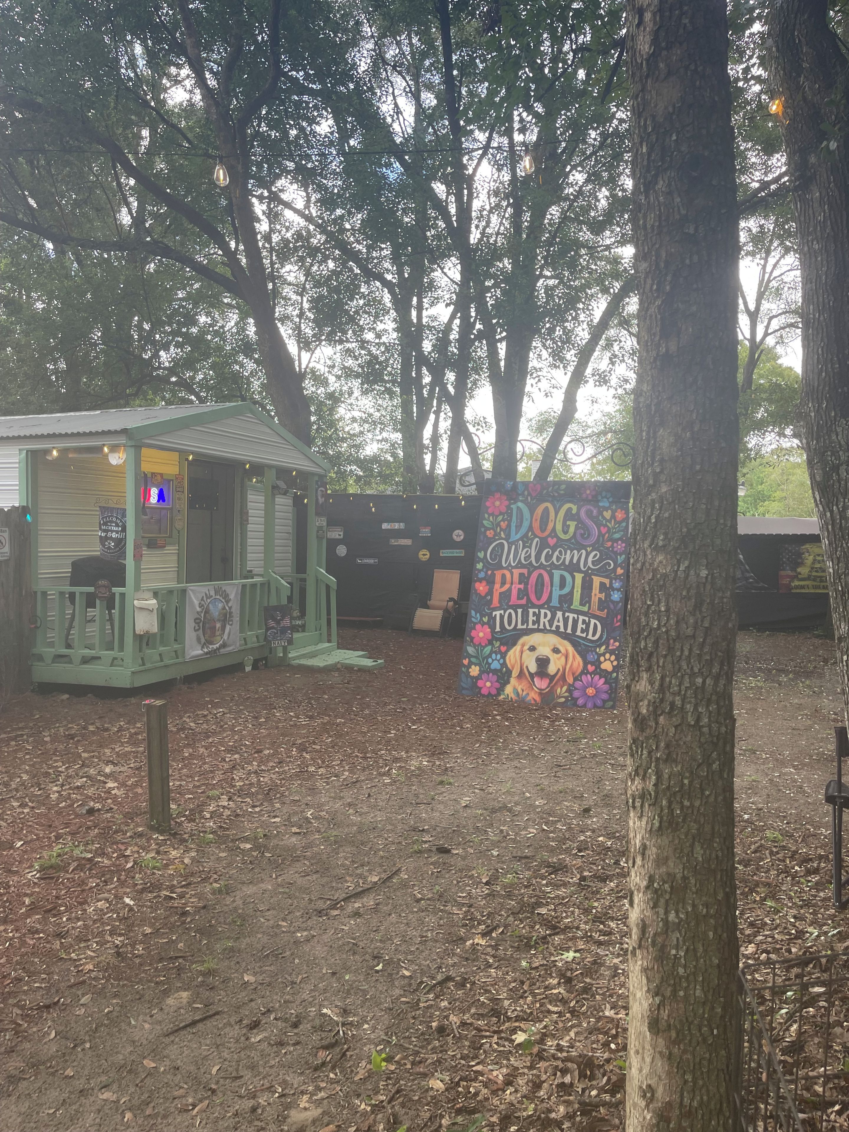 Een klein gebouw met een groen dak en een bord met een welkomstdrankje, omgeven door bomen.