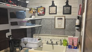 Een kleine keuken met een koffiezetapparaat, mokken, een spoelbak en een klein aanrecht.