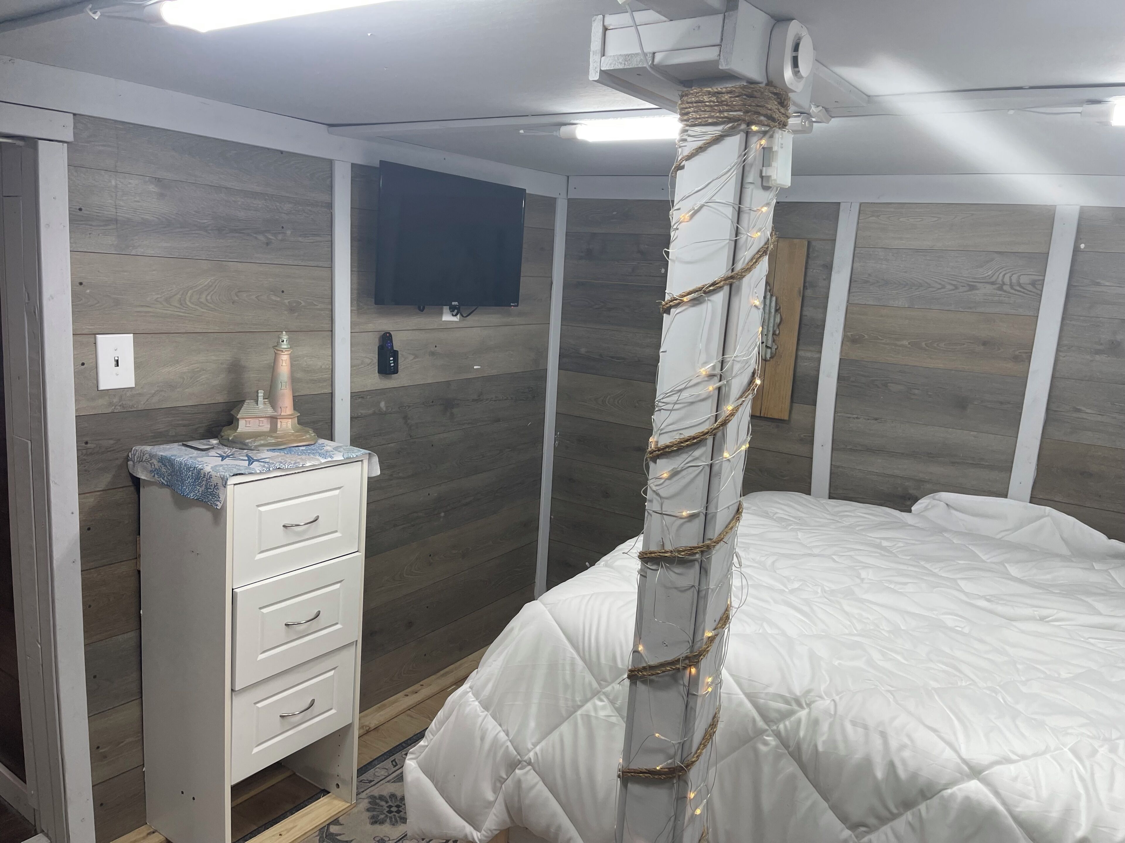 Quarto com cama, cômoda e televisão fixada na parede.