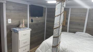 Quarto com cama, cômoda e televisão fixada na parede.