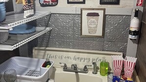 Een keuken met een spoelbak, een wijnglas, een afdruiprek, een mok in een lijst en popcorn dozen.
