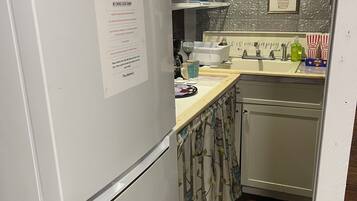 A kitchen with a white refrigerator, a sink, and a coffee machine. There is a note on the refrigerator, a patterned rug, and kitchen decorations on the wall.