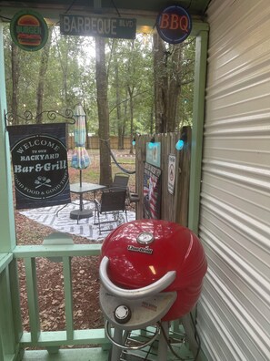 A BBQ grill outside a bar and grill with a sign welcoming visitors to the backyard. - Charming Rustic Tiny Home – Private 1 Ac Oasis - Yulee, FL (Yulee)