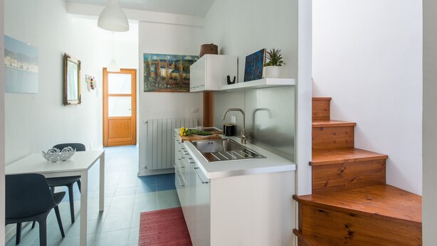 A compact kitchen with a built-in sink, a dining area with a table and chairs, and a staircase leading to another level. - Blue home in Vucciria (PALERMO)