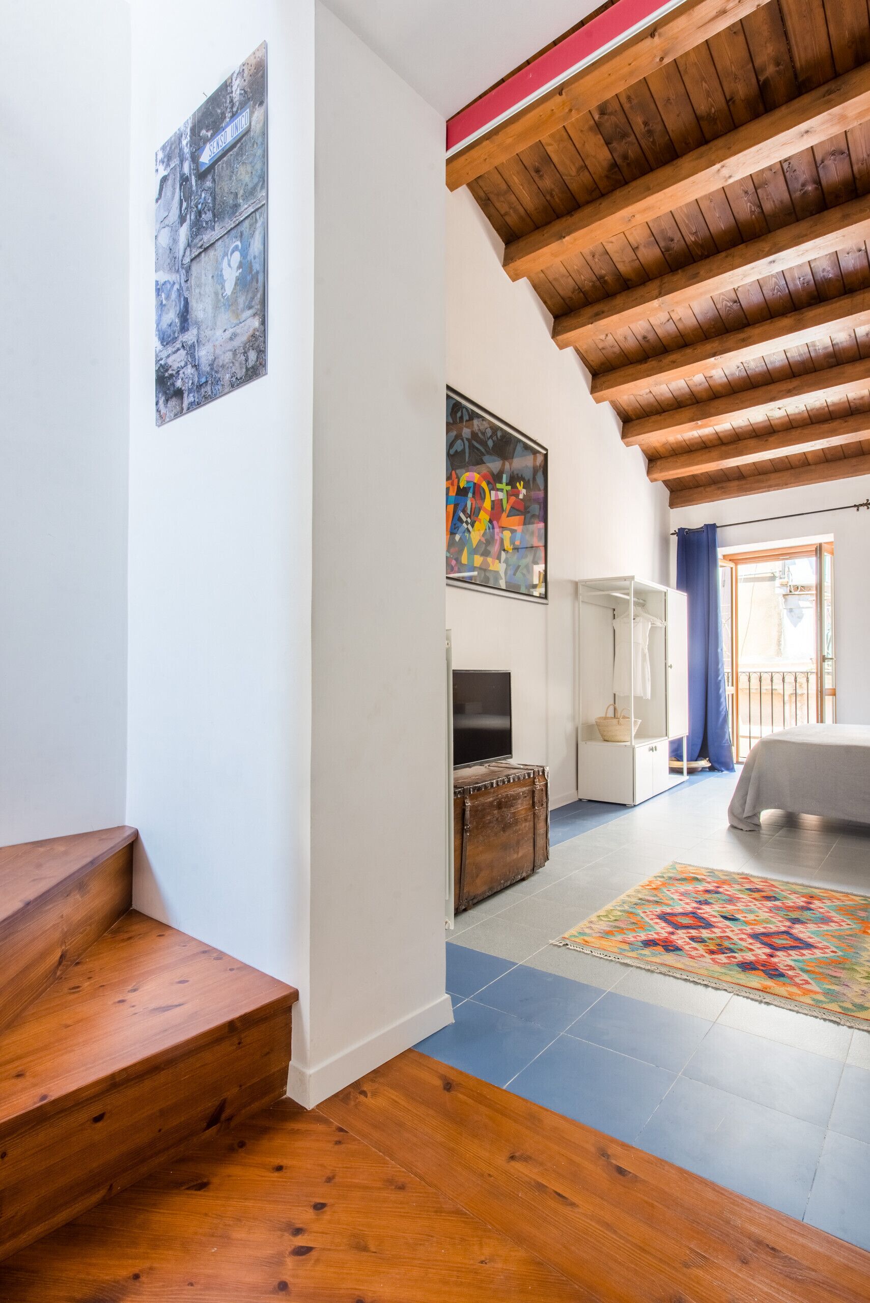 A staircase leading to a room with a television, a patterned rug, and a wooden ceiling.