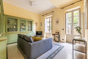 Ein Wohnzimmer mit einer Couch, Fernseher, grünen Schränken und einer Nähmaschine.