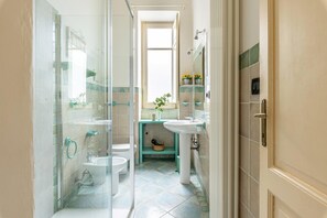 Ein Badezimmer mit Duschkabine aus Glas, Toilette, Waschbecken und einer kleinen Ablage für Toilettenartikel.