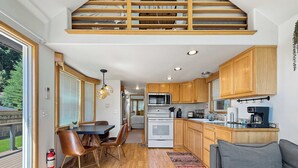 A compact kitchen with wooden cabinets, a dining area with a table and chairs, and a living room with a sofa. - Lake Sutherland Tiny Home, Heaven (Port Angeles)
