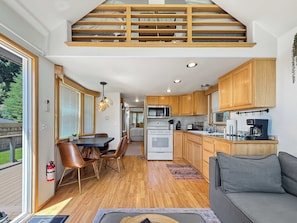 Eine kleine Küche mit Holzausstattung, ein Essbereich mit Tisch und Stühlen sowie ein Wohnzimmer mit einer Couch.