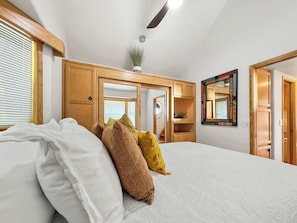 Ein Schlafzimmer mit einem Bett, Kissen, einem Spiegel, einem Deckenventilator und Holzmöbeln.