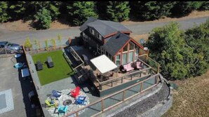 A two-story building with a deck, a covered outdoor seating area, and a fenced yard. - Lake Sutherland Tiny Home, Heaven (Port Angeles)