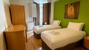 Habitación de hotel con dos camas, suelo de madera, pared decorada en verde, un cuadro y una araña.