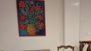 Un área de comedor con una mesa de madera y dos sillas, una estantería y un cuadro con motivos florales en la pared.
