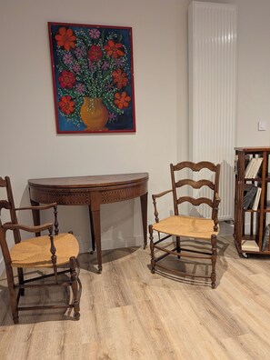 Un área de comedor con una mesa de madera y dos sillas, una estantería y un cuadro con motivos florales en la pared.