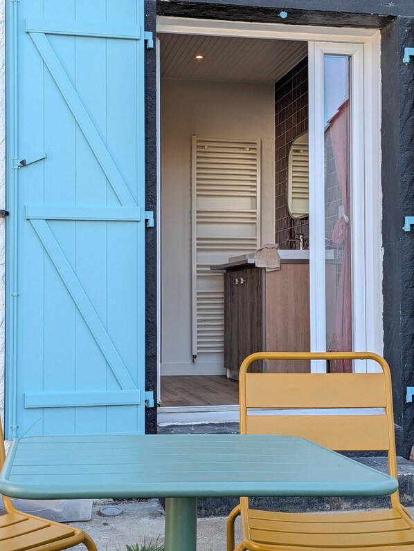 A blue door leading to a room with a kitchen, a dining table with yellow chairs, and a window with a curtain. - Maison Millefeuille (Saint-Hilaire-de-Riez)