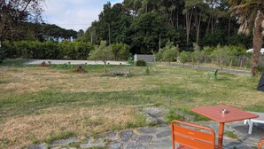 Un patio de piedra con una mesa y banca de metal, rodeado de césped y árboles.