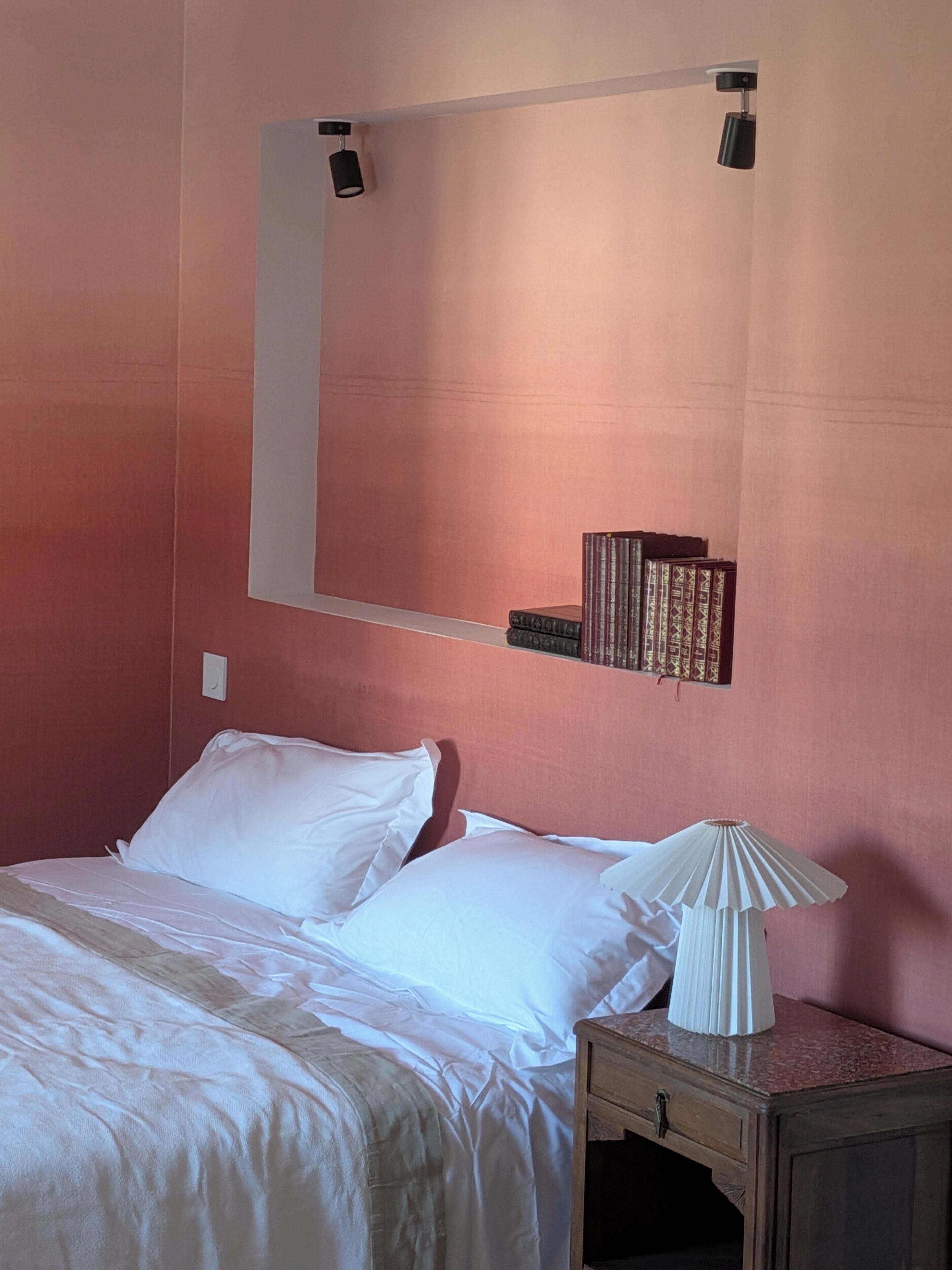 Une chambre à coucher comprenant un lit, une table de chevet, une lampe et un miroir fixé au mur.