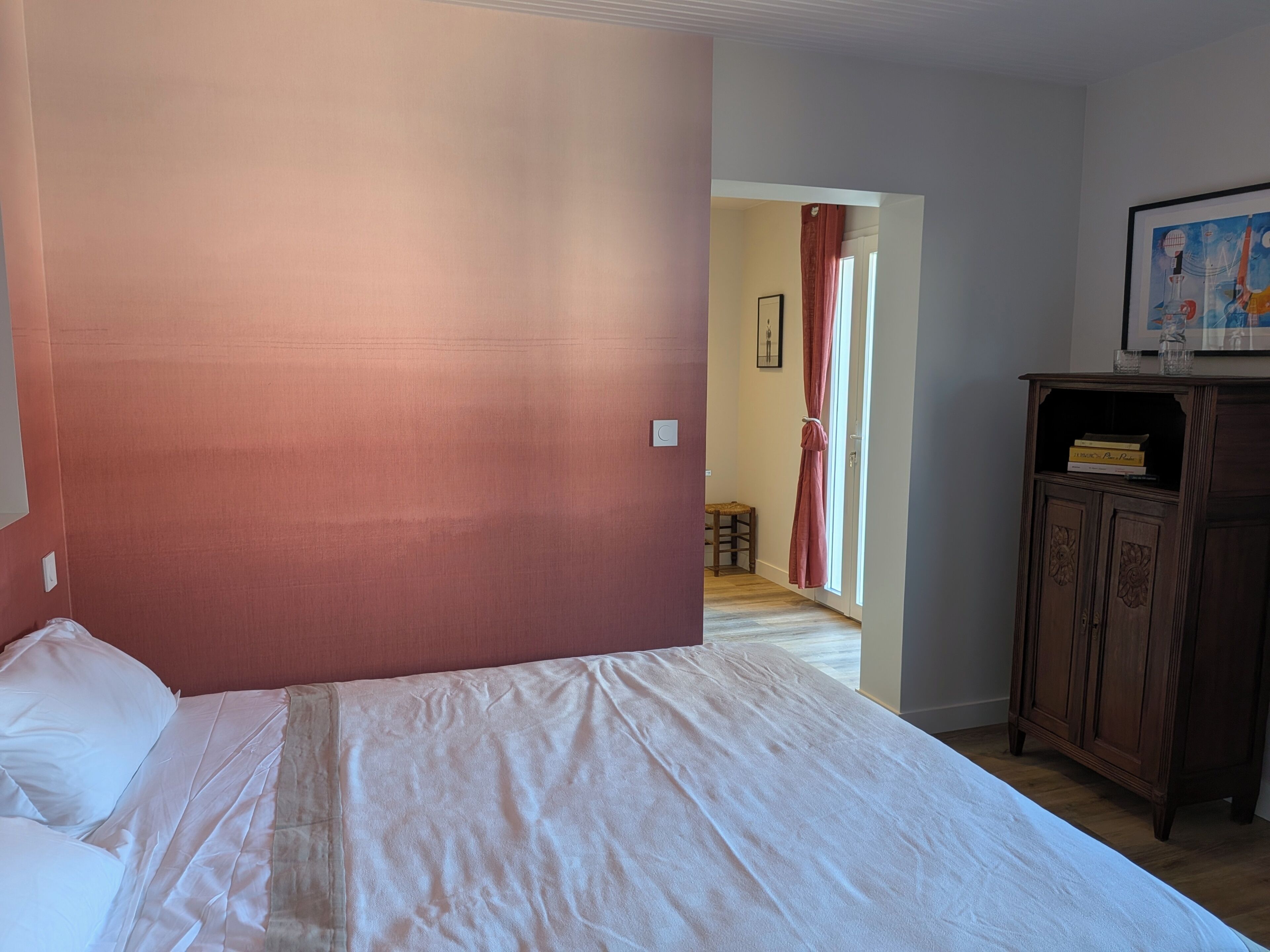 Une chambre à coucher avec un lit, une armoire en bois et une porte donnant sur une autre pièce.