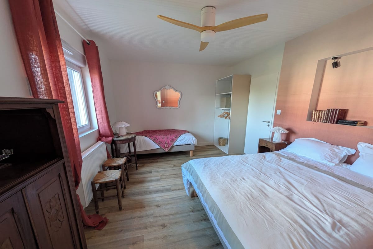 A bedroom with a bed, a desk, a chair, a wardrobe, a ceiling fan, and a window with curtains.