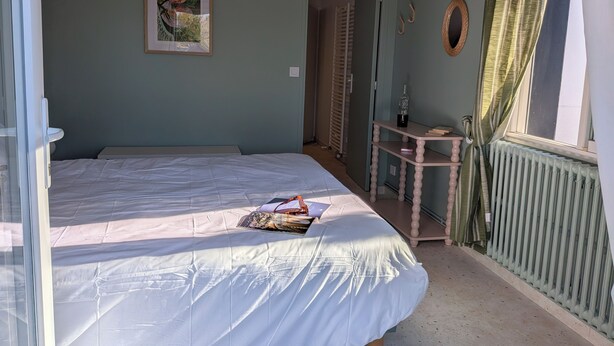 Un dormitorio con una cama, una mesita de noche con una botella, un cuadro enmarcado y una ventana con cortinas.