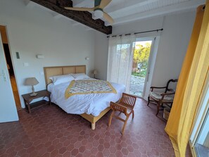 A bedroom with a bed, a chair, a nightstand, a lamp, and a window with curtains. - Maison Millefeuille  (Saint-Hilaire-de-Riez)