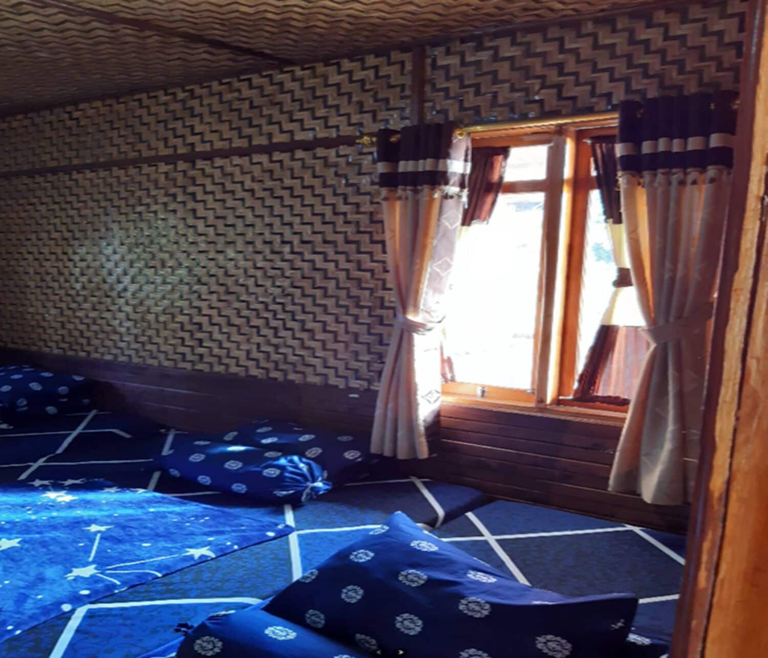 Una habitación con un papel tapiz estampado, una ventana con cortinas y un felpudo azul con motivos de estrellas.
