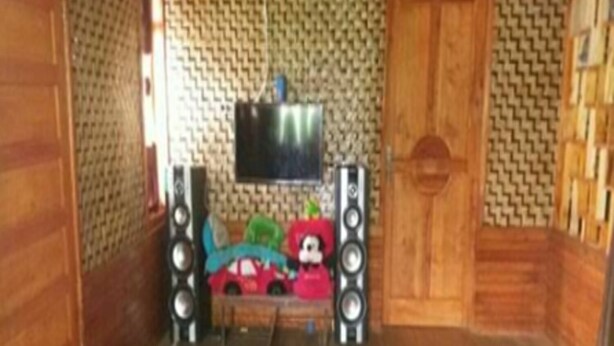 Una habitación con piso de madera, un televisor montado en la pared y una mesita con un coche de juguete y una figura.