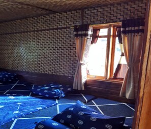Una habitación con pared estampada, ventana con cortinas y un felpudo azul con almohadones.