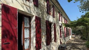 Ein Steinhaus mit roten Fensterläden, einer kleinen Außen-Sitzgelegenheit und einem Kiesweg.