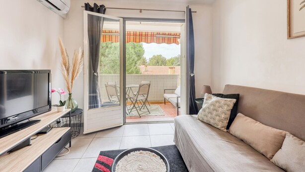 A modern living room with a flat-screen TV, sofa, and a balcony with outdoor furniture. - Fabregas - Proche plage - Petfriendly (La Seyne-sur-Mer)