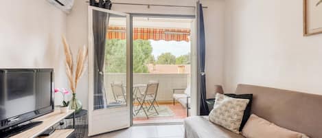 A modern living room with a flat-screen TV, sofa, and a balcony with outdoor furniture.