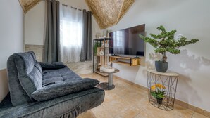 Ein Wohnzimmer mit grauem Sofa, einem an der Wand befestigten Fernseher, einem Bonsai-Baum im Topf und einem kleinen runden Tisch.