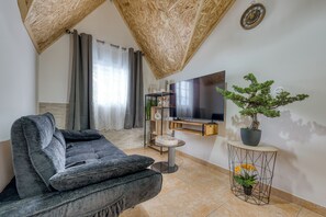 Ein Wohnzimmer mit grauem Sofa, einem an der Wand befestigten Fernseher, einem Bonsai-Baum im Topf und einem kleinen runden Tisch.