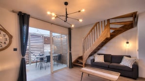 A living room with a wooden staircase, a sofa, a dining table, and a large window. - Petit Duc - AC - Patio - Wifi (Saint-Paul)