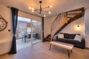 Ein Wohnzimmer mit einer Holztreppe, einem Sofa, einem Esstisch und einem großen Fenster.