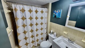 A bathroom with a shower curtain, toilet, sink, and a painting on the wall. - Family-friendly 4-bedroom apartment in the historic North End of Boston (Boston)